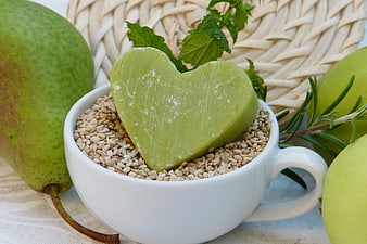 Heart-shaped green soap in cup with sesame seeds and fruit
