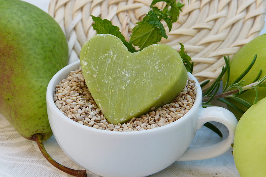 Heart-shaped green soap in cup with sesame seeds and fruit