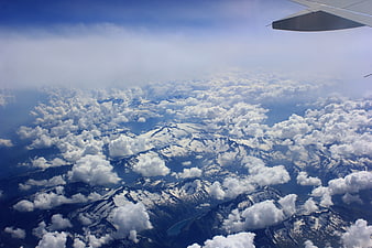 Aerial View of Snowy Mountains Through Clouds from Airplane Window