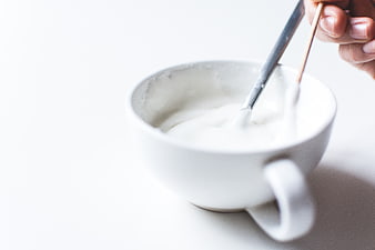 Hand mixing white icing in a white ceramic cup
