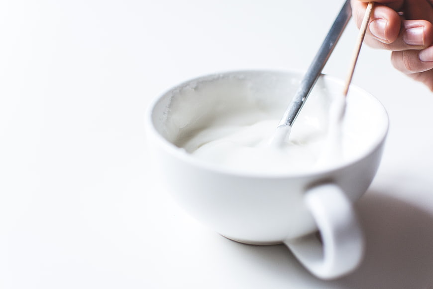 Hand mixing white icing in a white ceramic cup