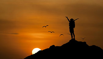 Silhouette of hiker with raised arms on mountain peak at sunset
