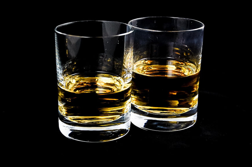 Two glasses of amber whiskey on a black background