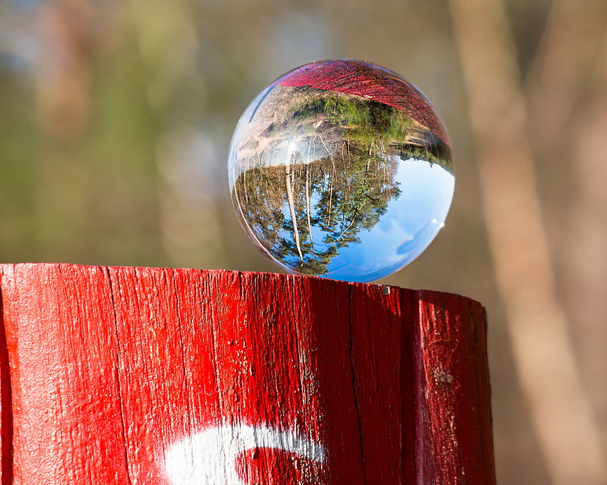 Glass Crystal Ball on Red Wooden Post Reflecting Forest Landscape