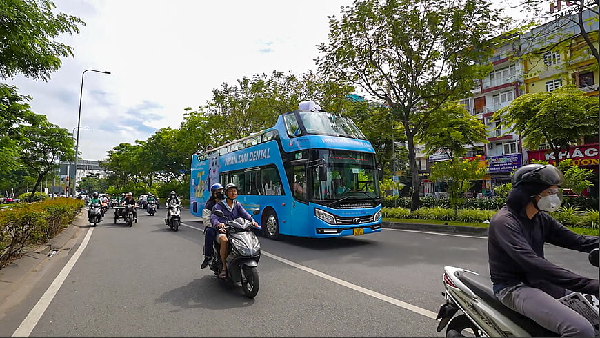 Blue double-decker bus and motorbikes on busy city street