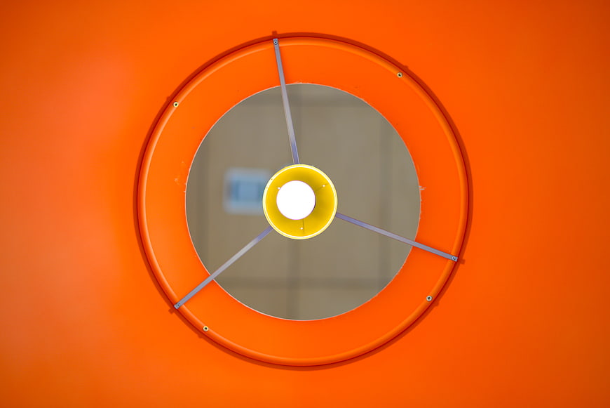 Orange circular lamp shade with yellow bulb and metal supports