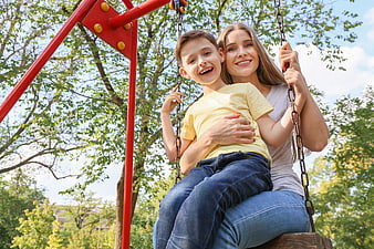 Happy Mother and Son Laughing Together on a Park Swing