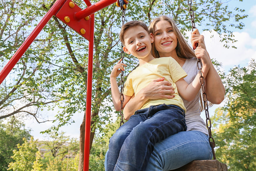 Happy Mother and Son Laughing Together on a Park Swing