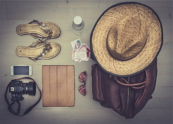 Flat lay of travel essentials including straw hat, camera, and sandals