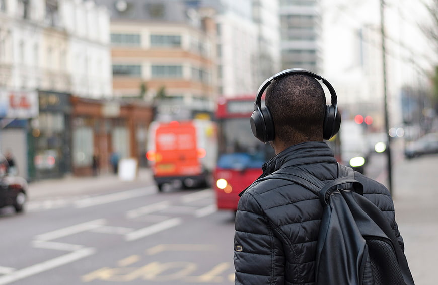 Man with headphones and backpack on busy city street