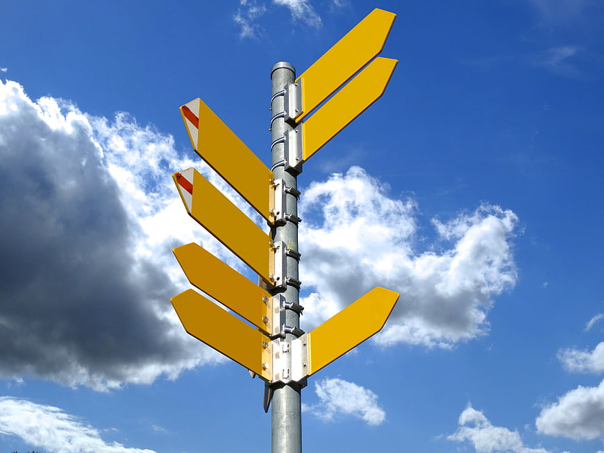 Yellow Directional Signpost Arrows Against Blue Sky And Clouds