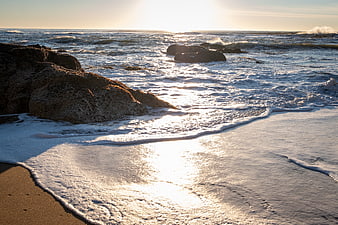Sunlit ocean waves crashing on rocky beach at sunset