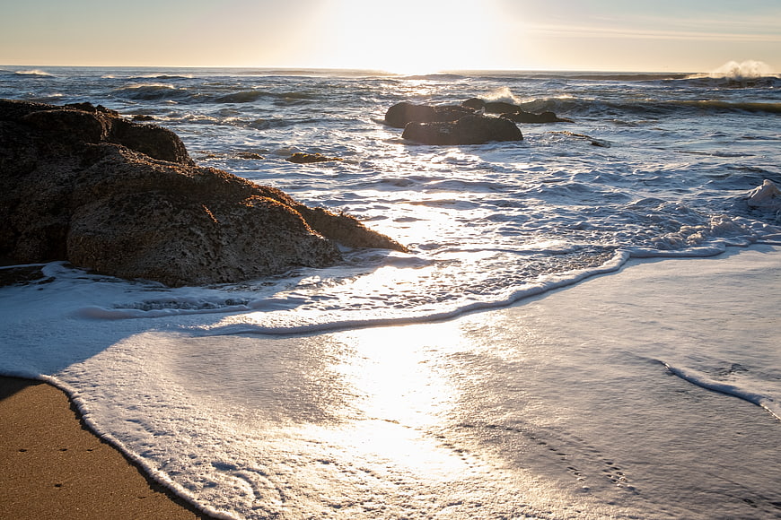 Sunlit ocean waves crashing on rocky beach at sunset