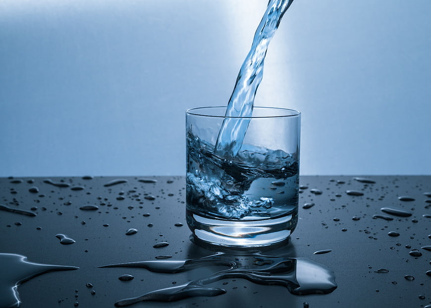 Water Pouring into Glass with Splashes on Dark Surface
