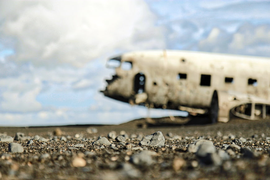 Low angle view of rocky ground with blurred airplane wreck in background