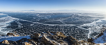 Panoramic view of frozen lake with cracked ice and rocky foreground