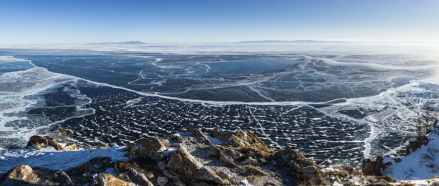 Panoramic view of frozen lake with cracked ice and rocky foreground