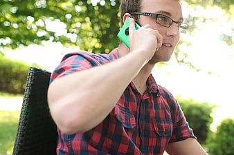 Man in plaid shirt talking on green smartphone outdoors