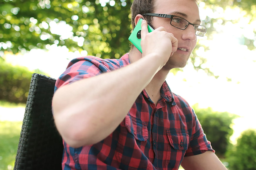 Man in plaid shirt talking on green smartphone outdoors