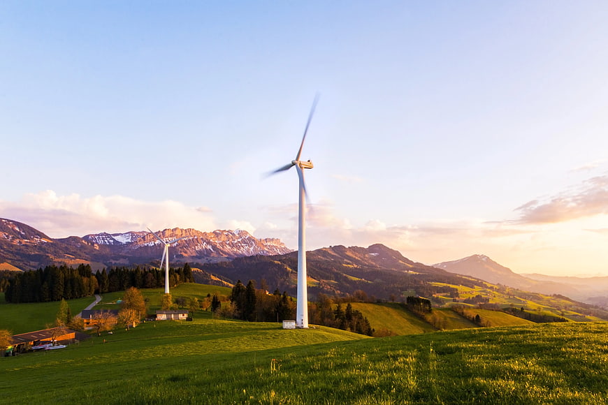 Wind turbines on green hills with mountains at sunset