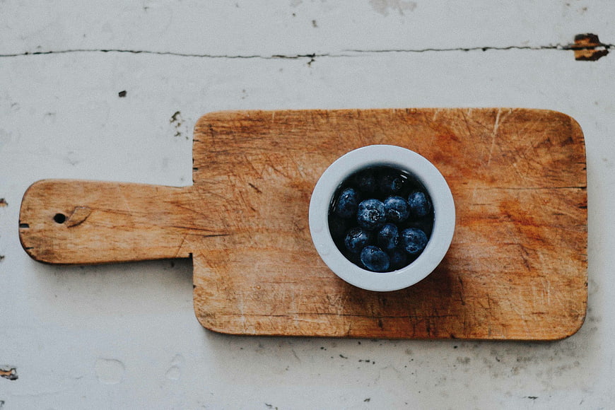 Top view of fresh blueberries in a white bowl on a wooden board