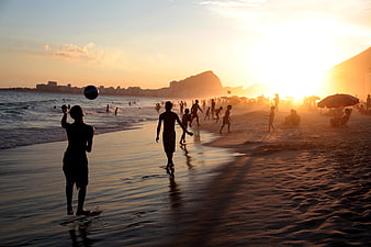 Silhouettes of people playing soccer on beach at sunset