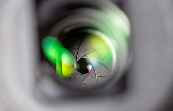 Close-up of camera lens aperture with green bokeh reflections