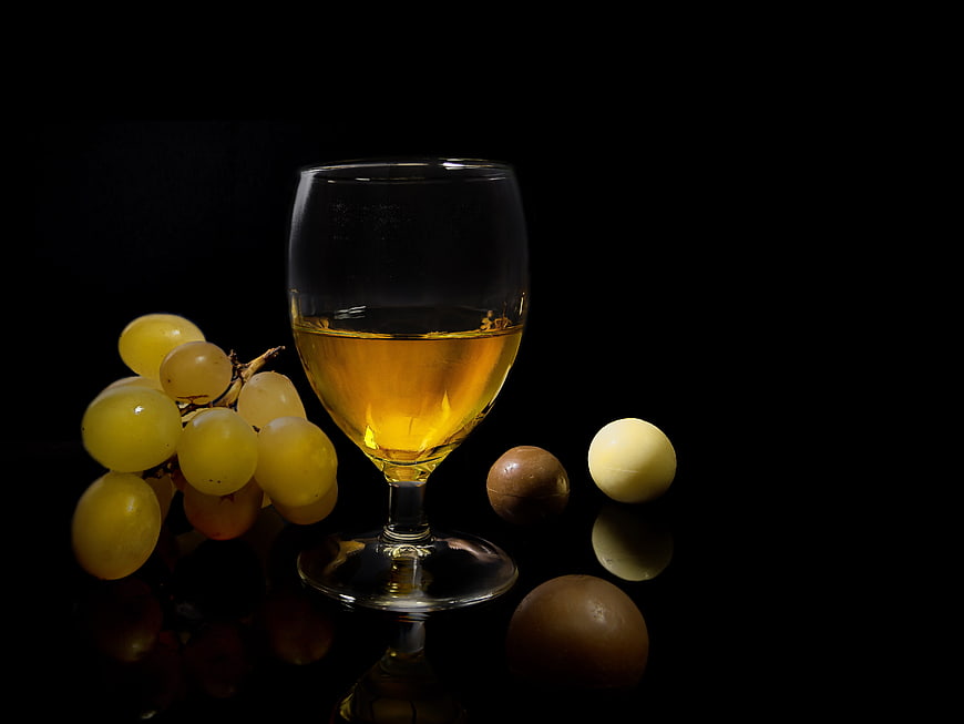 Glass of white wine with grapes and chocolates on black background