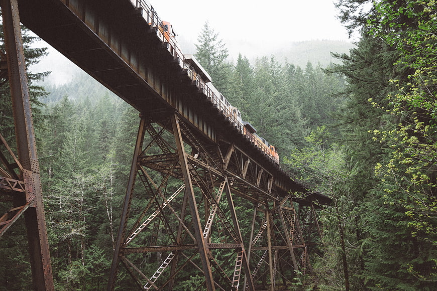 Orange train crossing high steel trestle bridge in forest