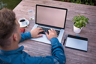 Man working on laptop at outdoor wooden table with coffee