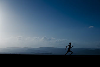 Silhouette of Man Running Against Blue Mountain Sky