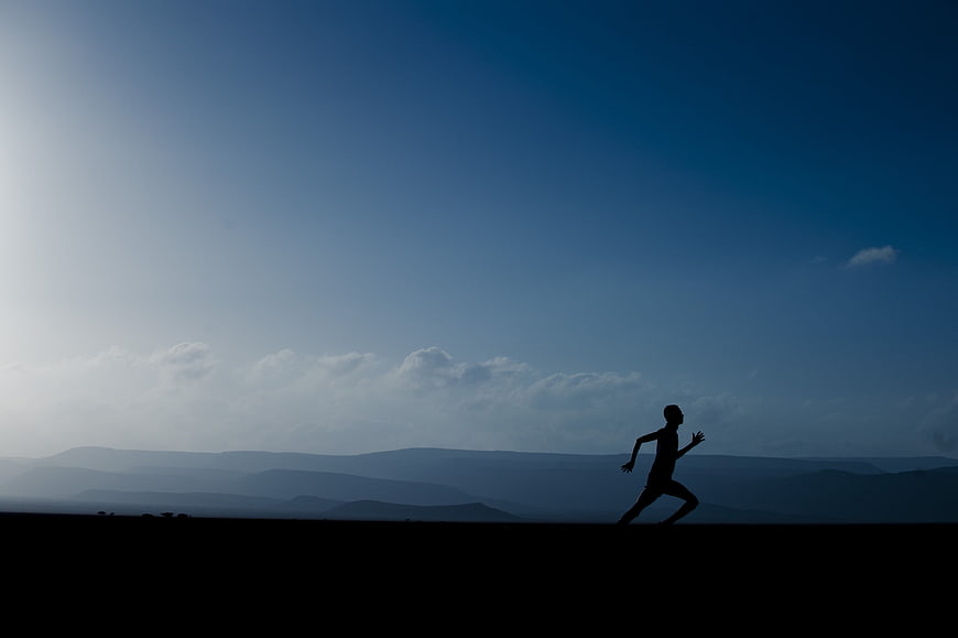 Silhouette of Man Running Against Blue Mountain Sky