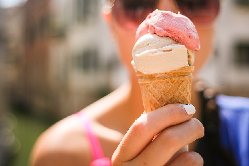 Woman holding strawberry and vanilla ice cream cone outdoors