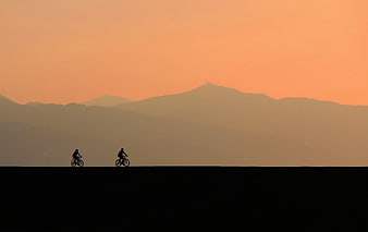 Silhouette of Two Cyclists Riding Against Orange Sunset Sky