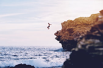 Man cliff diving into ocean waves at sunset