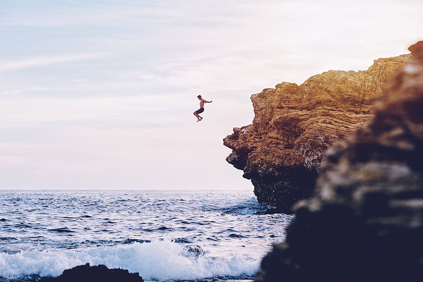 Man cliff diving into ocean waves at sunset