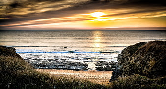 Dramatic Sunset Over Rocky Coastal Beach with Golden Sky