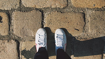 Top-down view of white sneakers on cobblestone pavement