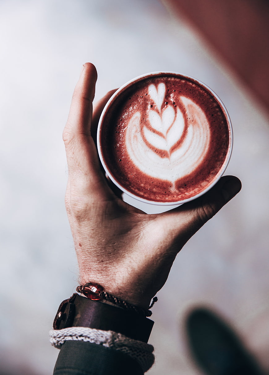Hand holding latte with leaf art top down view