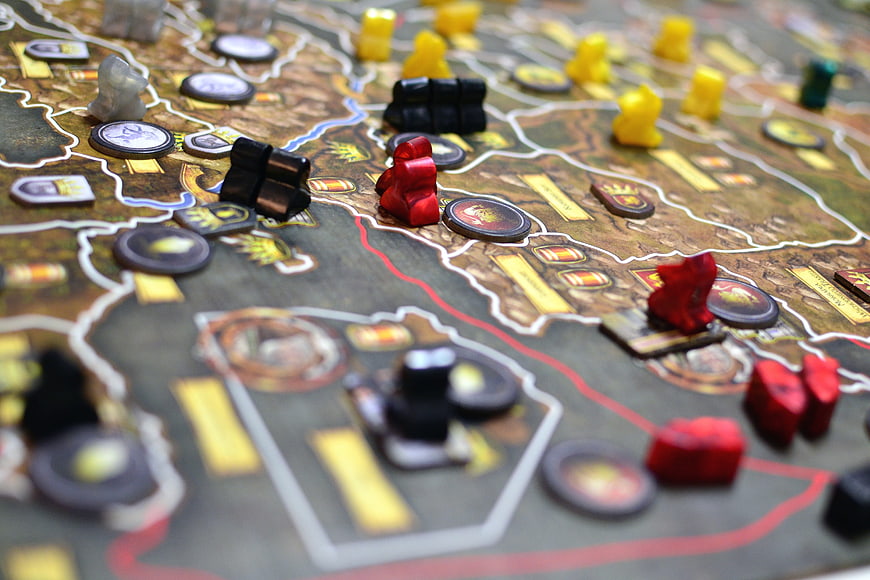 Close-up of a strategy board game with red, black, and yellow pawns