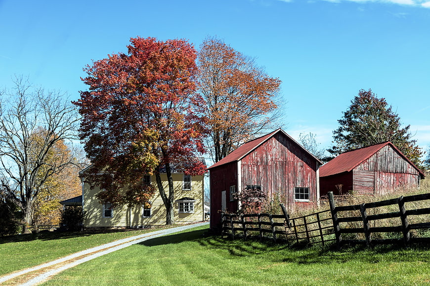Rustic Red Barn And Farmhouse With Autumn Trees In Rural Landscape