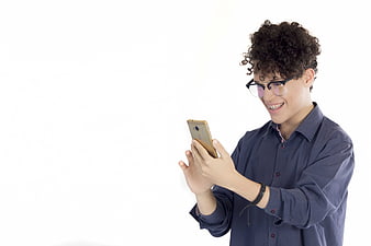 Young man with curly hair and glasses smiling while using a smartphone