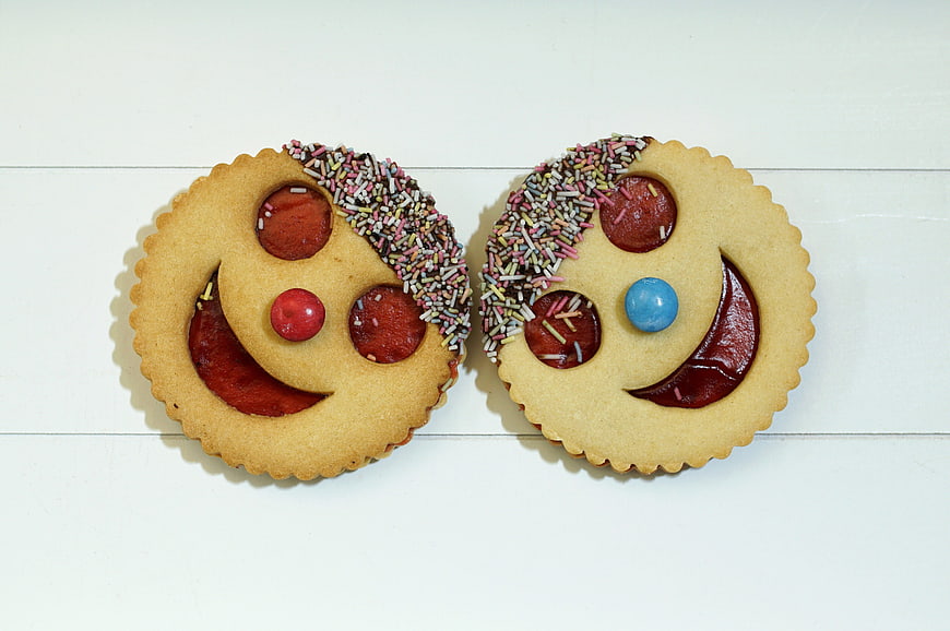 Two decorated smiley face cookies with jam and sprinkles