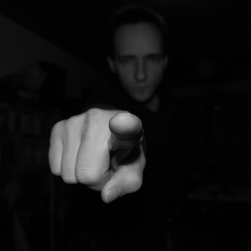 Man Pointing Finger Directly at Camera in Dark Room