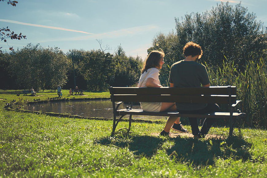 Couple Sitting on Park Bench by Pond in Sunlight