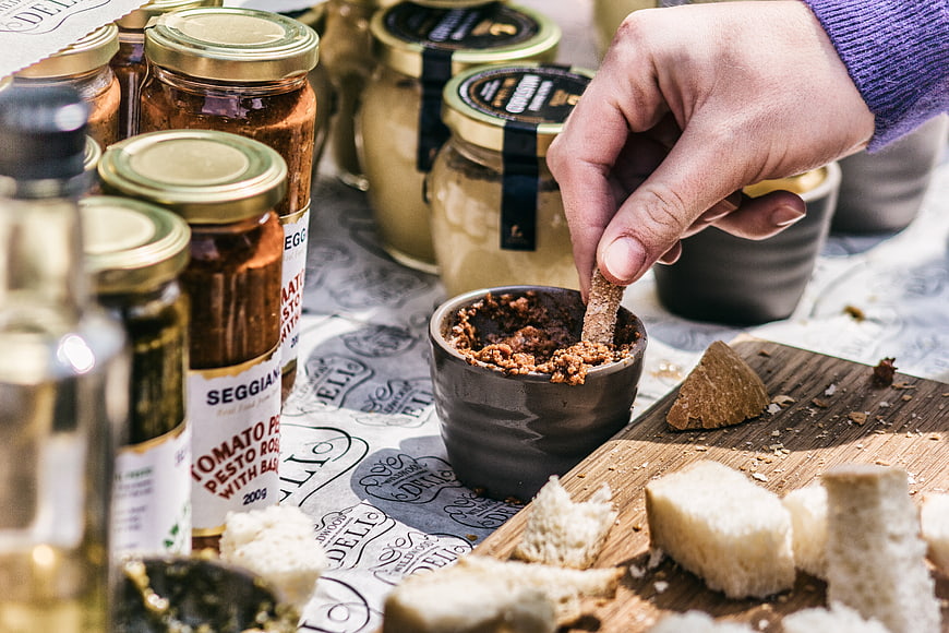 Hand dipping bread into rustic tomato pesto spread