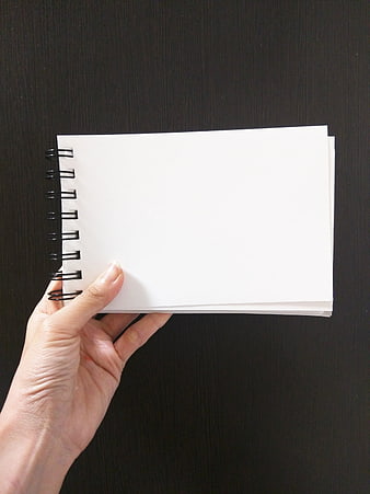 Hand holding blank white spiral notebook against dark background