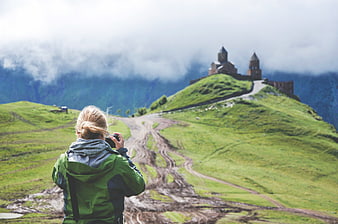 Woman Photographing Mountain Church in Green Landscape