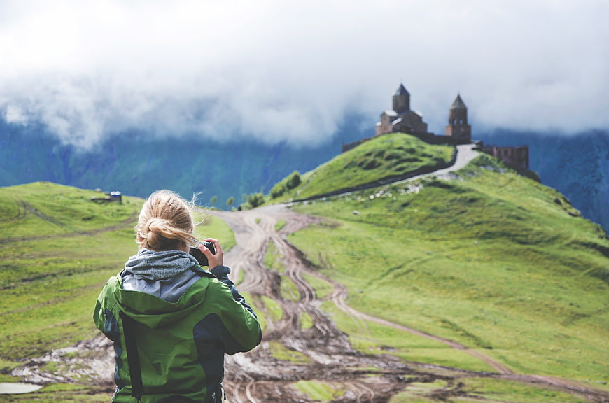 Woman Photographing Mountain Church in Green Landscape