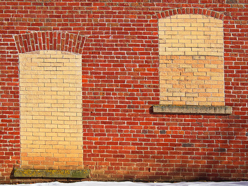 Red brick wall with bricked-up windows and stone sills